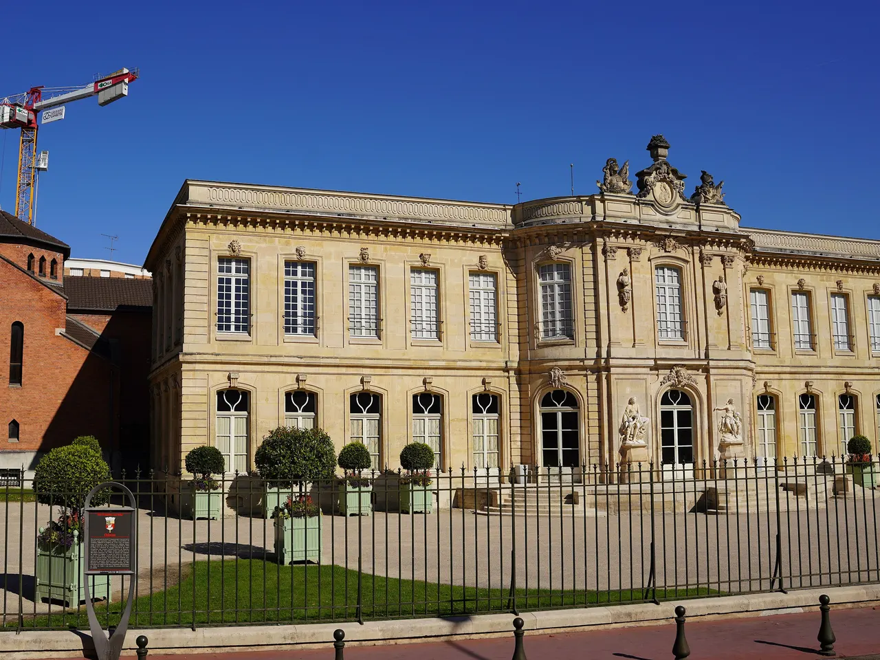 Le château d’Asnières, sa façade de pierre blonde et son fronton sculpté, derrière une grille, sous un ciel bleu