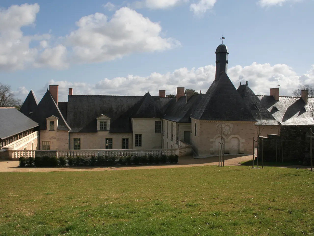 Le château de la Perrière à Avrillé, logis de pierre claire aux hauts toits d’ardoise et tourelle coiffée d’un lanternon, au bout d’une pelouse.