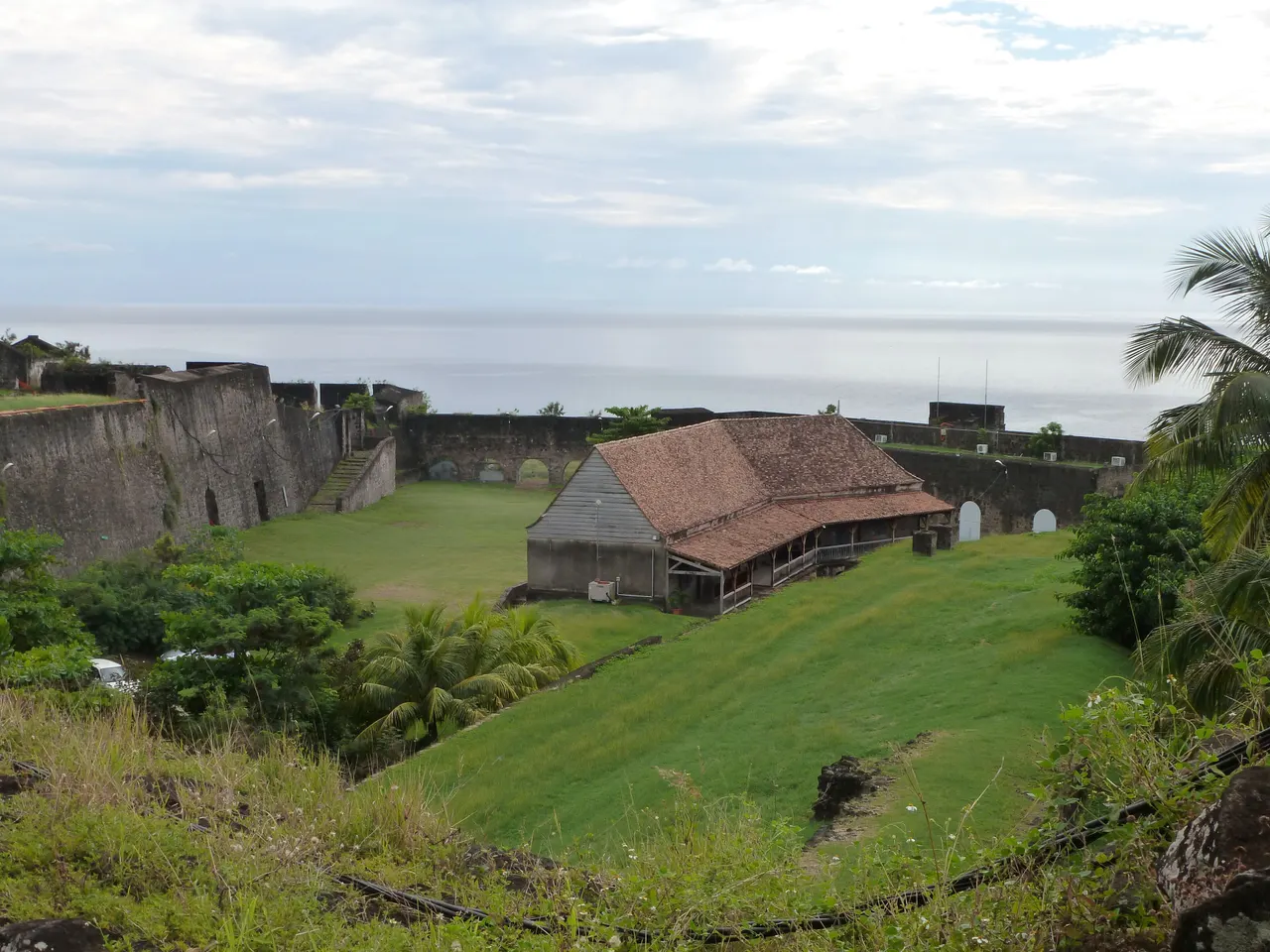 Le fort Delgrès à Basse-Terre : remparts de pierre, pelouses en contrebas et bâtiment au toit brun, avec la mer des Caraïbes à l’horizon.