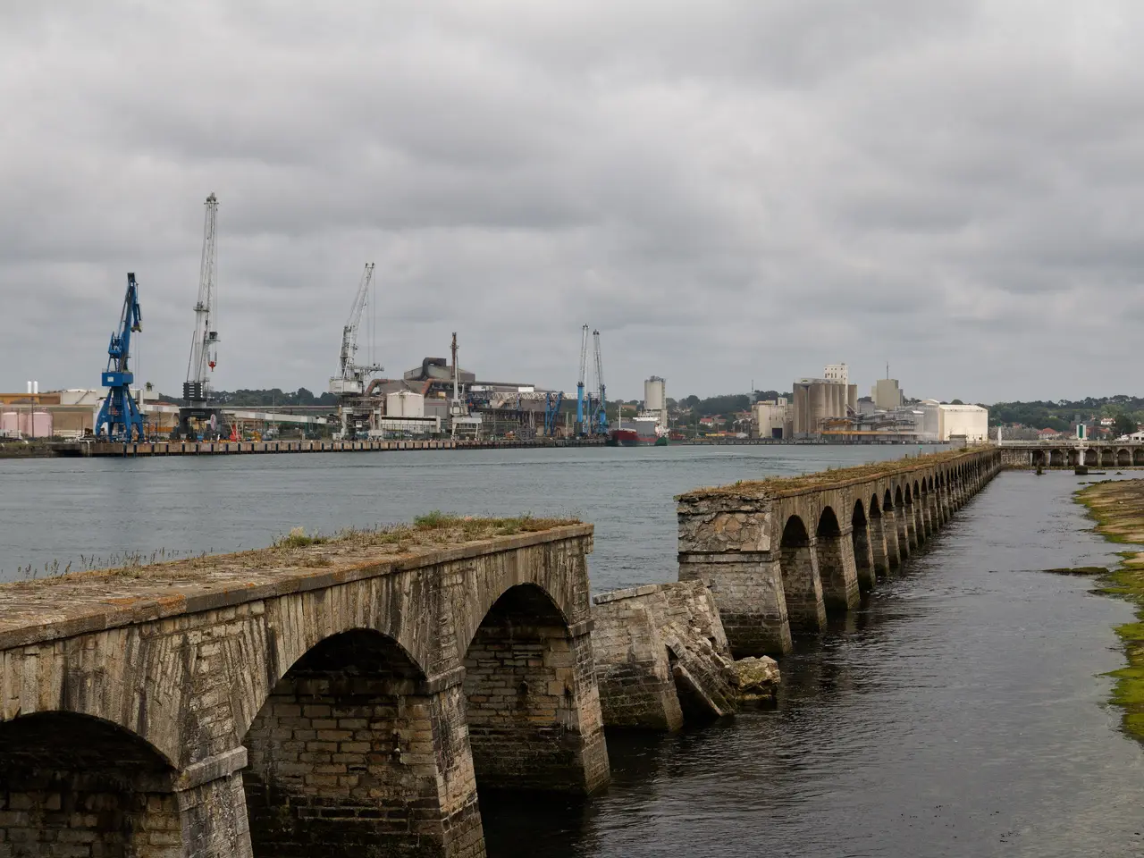 Les arches de pierre d’un ancien ouvrage le long de la rive droite de l’Adour, au Boucau, avec les grues du port à l’arrière-plan