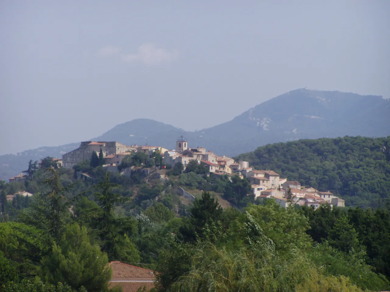 Le vieux village de Cabriès perché sur son piton, avec son château et son clocher, devant des collines boisées dans une lumière brumeuse.