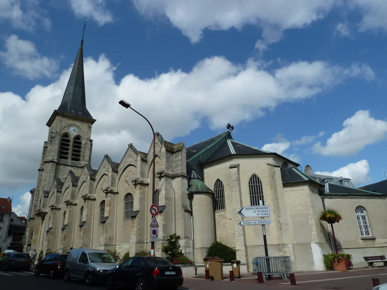 L’église Saint-Philippe-et-Saint-Jacques de Châtillon, son clocher pointu et son chevet, au bord d’une rue sous un ciel nuageux.