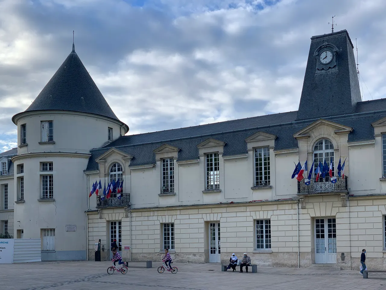 L’hôtel de ville de Clamart, sa tour ronde au toit conique et son pavillon à horloge pavoisé, sur une place dallée.