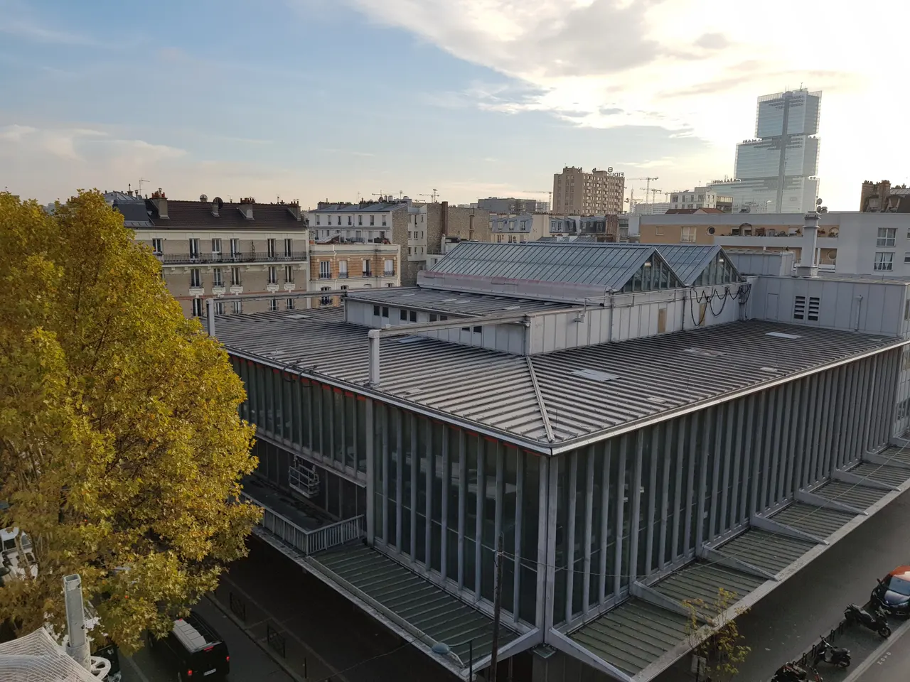 La Maison du Peuple de Clichy vue d’en haut, sa longue façade de métal et ses verrières, avec la tour du tribunal de Paris à l’horizon