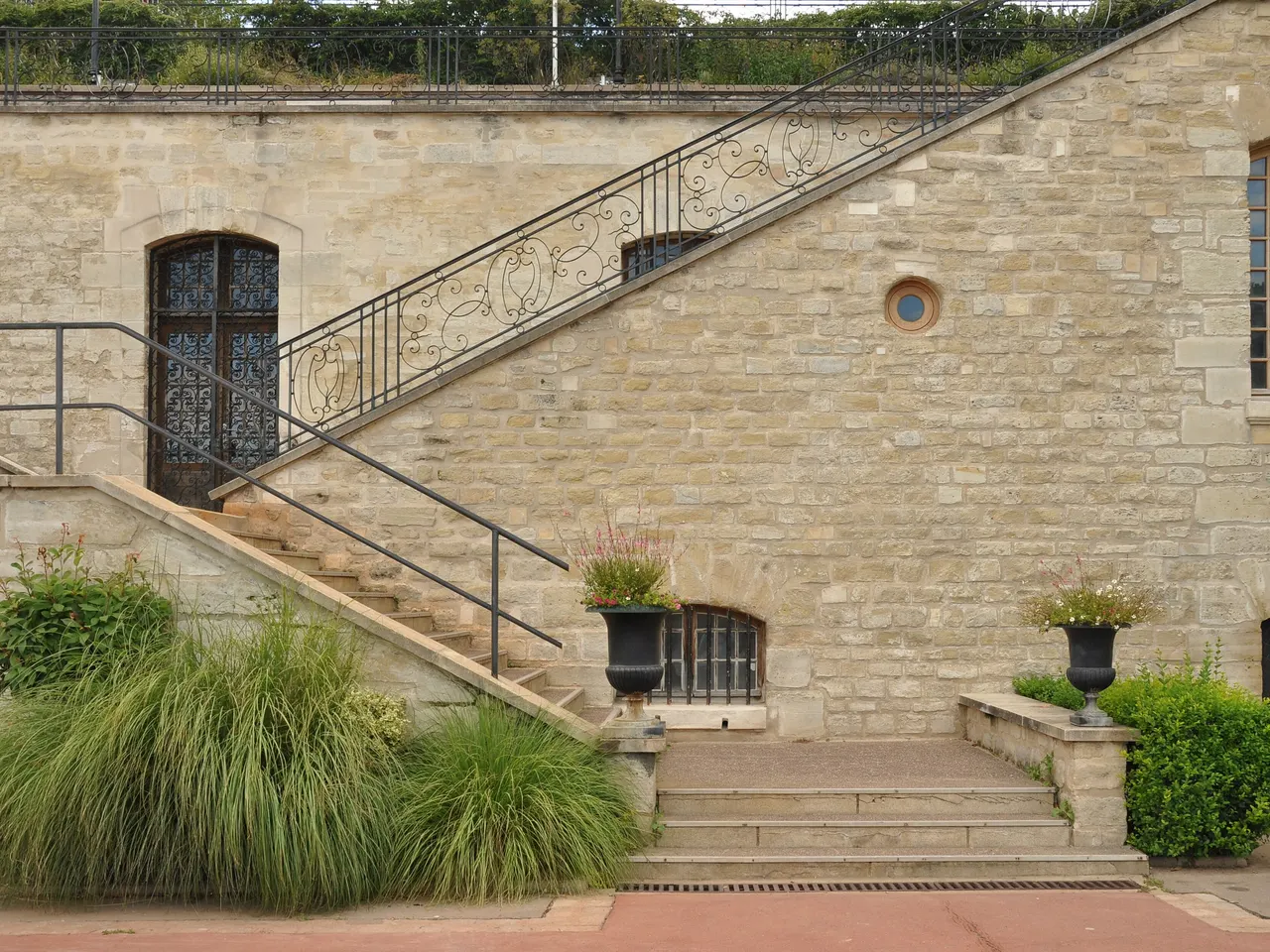 L’escalier monumental en pierre blonde du parc de Bécon, à Courbevoie, avec sa rampe en fer forgé, ses vasques fleuries et des touffes de graminées.