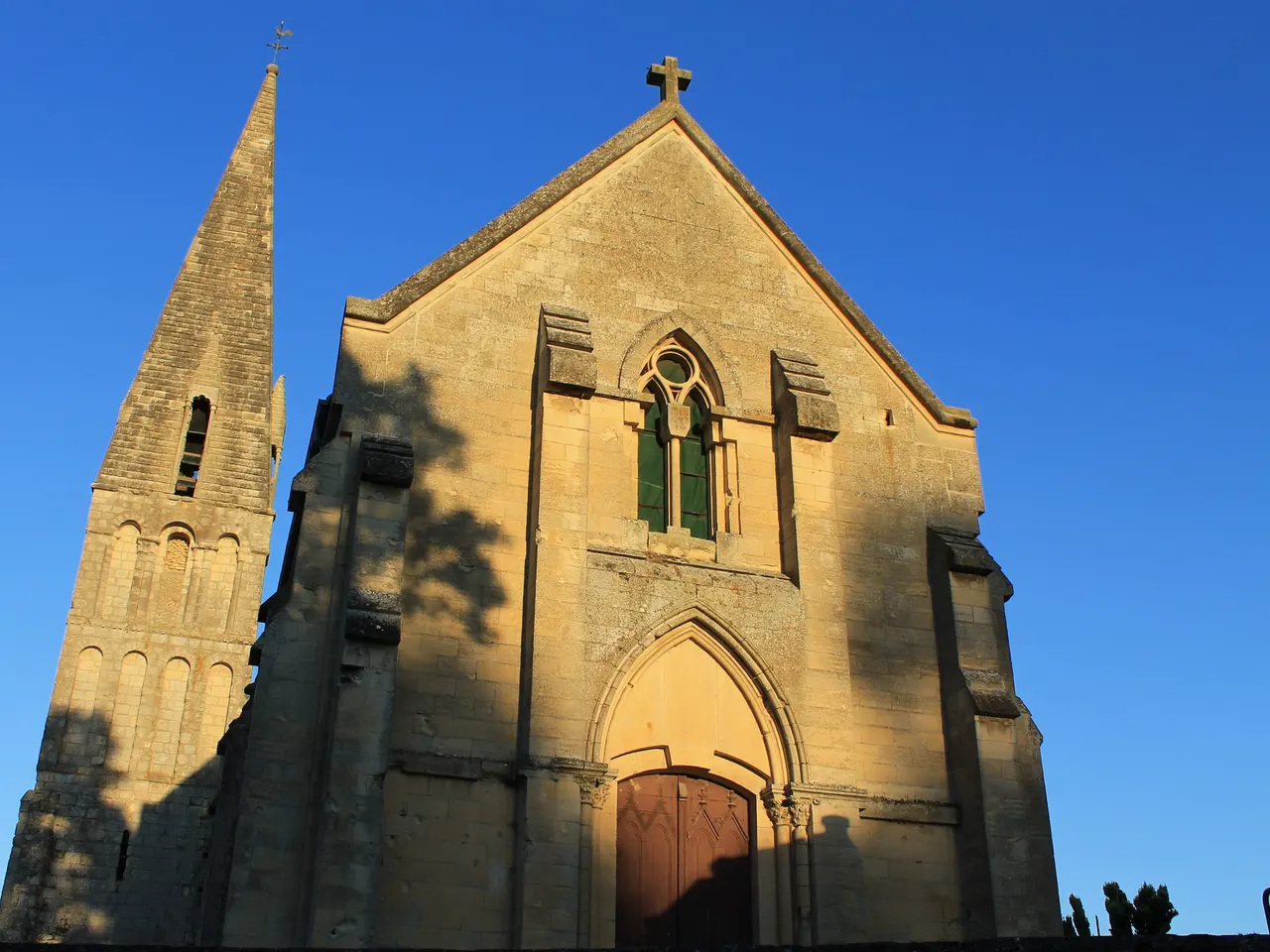 Le clocher roman en flèche et la façade néogothique de l’église Notre-Dame de Basse-Allemagne, à Fleury-sur-Orne, sous un ciel bleu