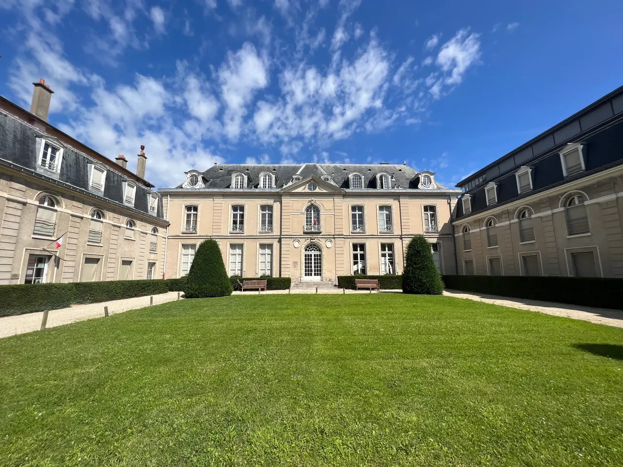 Le château Sainte-Barbe à Fontenay-aux-Roses, façade classique au toit d’ardoise entre deux ailes, devant une pelouse et deux ifs taillés en pointe.