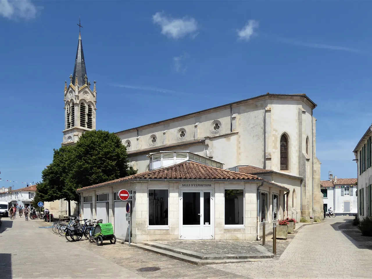 L’église néo-gothique Notre-Dame-de-l’Annonciation de La Couarde-sur-Mer et sa haute flèche, au bord d’une rue pavée du centre du village.
