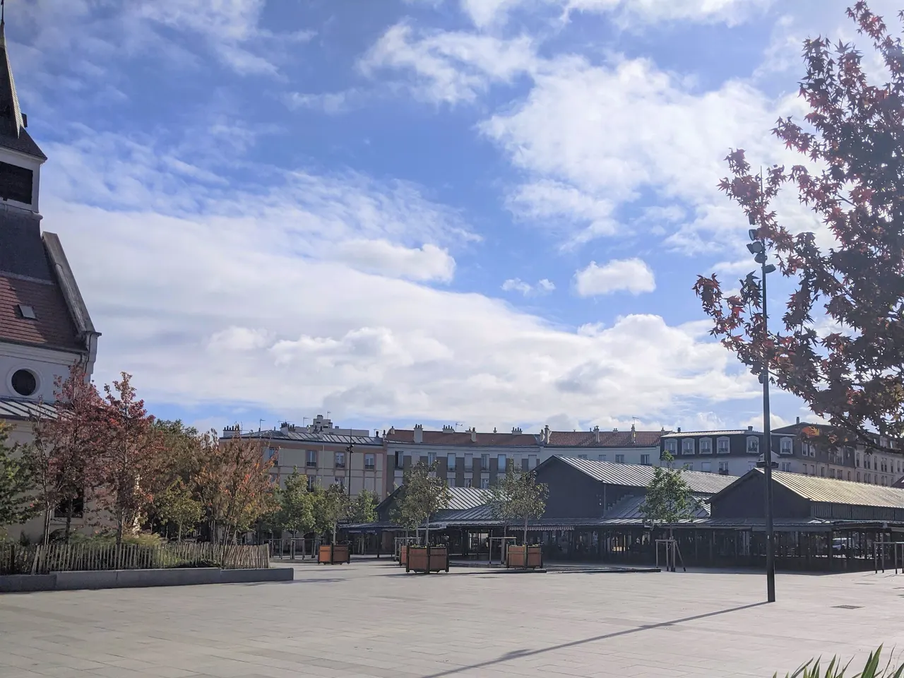 La place de la Liberté à La Garenne-Colombes, avec la halle du marché, des arbres aux feuilles rougies et le clocher de l’église Saint-Urbain.