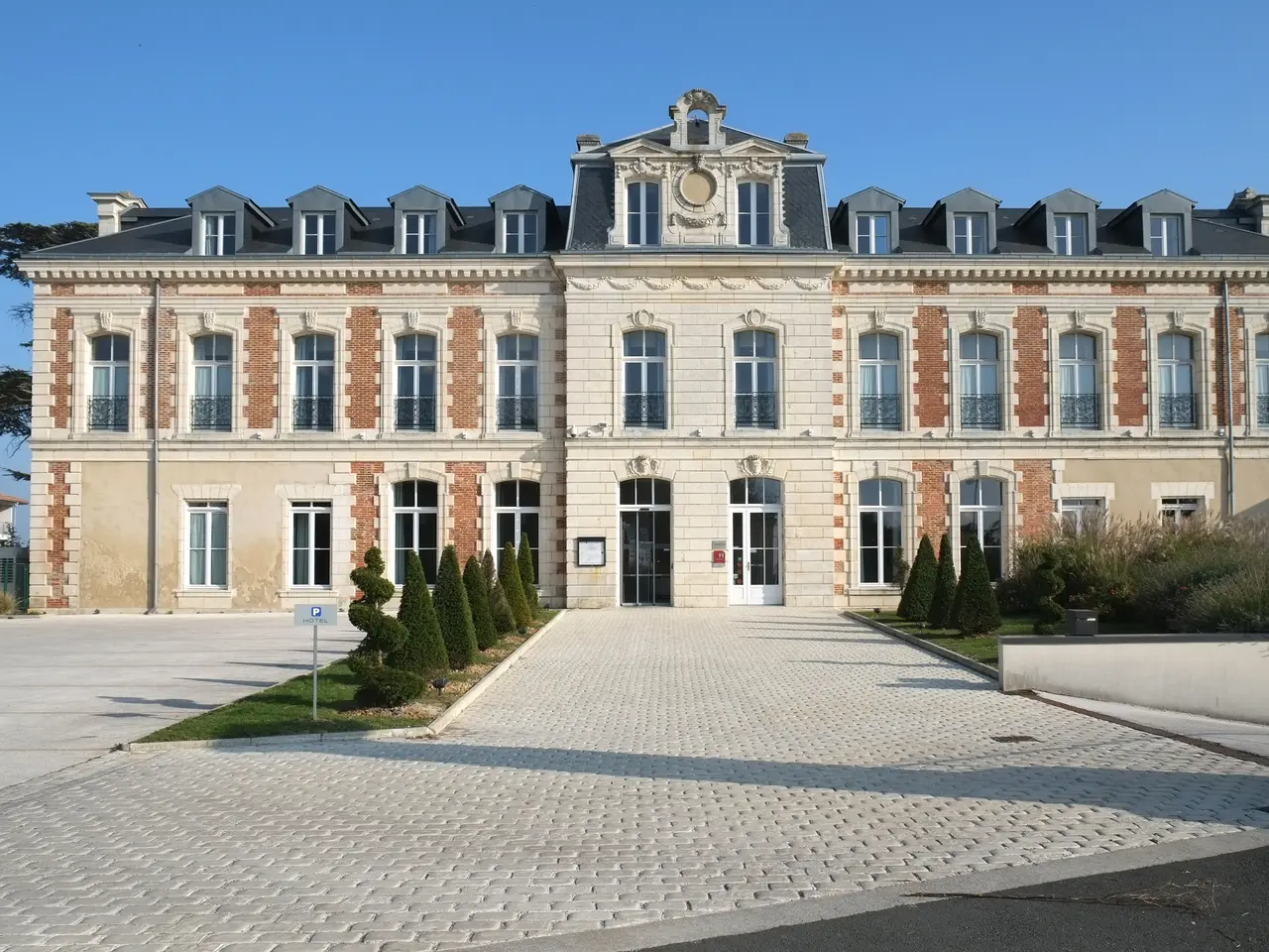 La façade de pierre et de brique du château du Clavier, à Lagord, devant une cour pavée