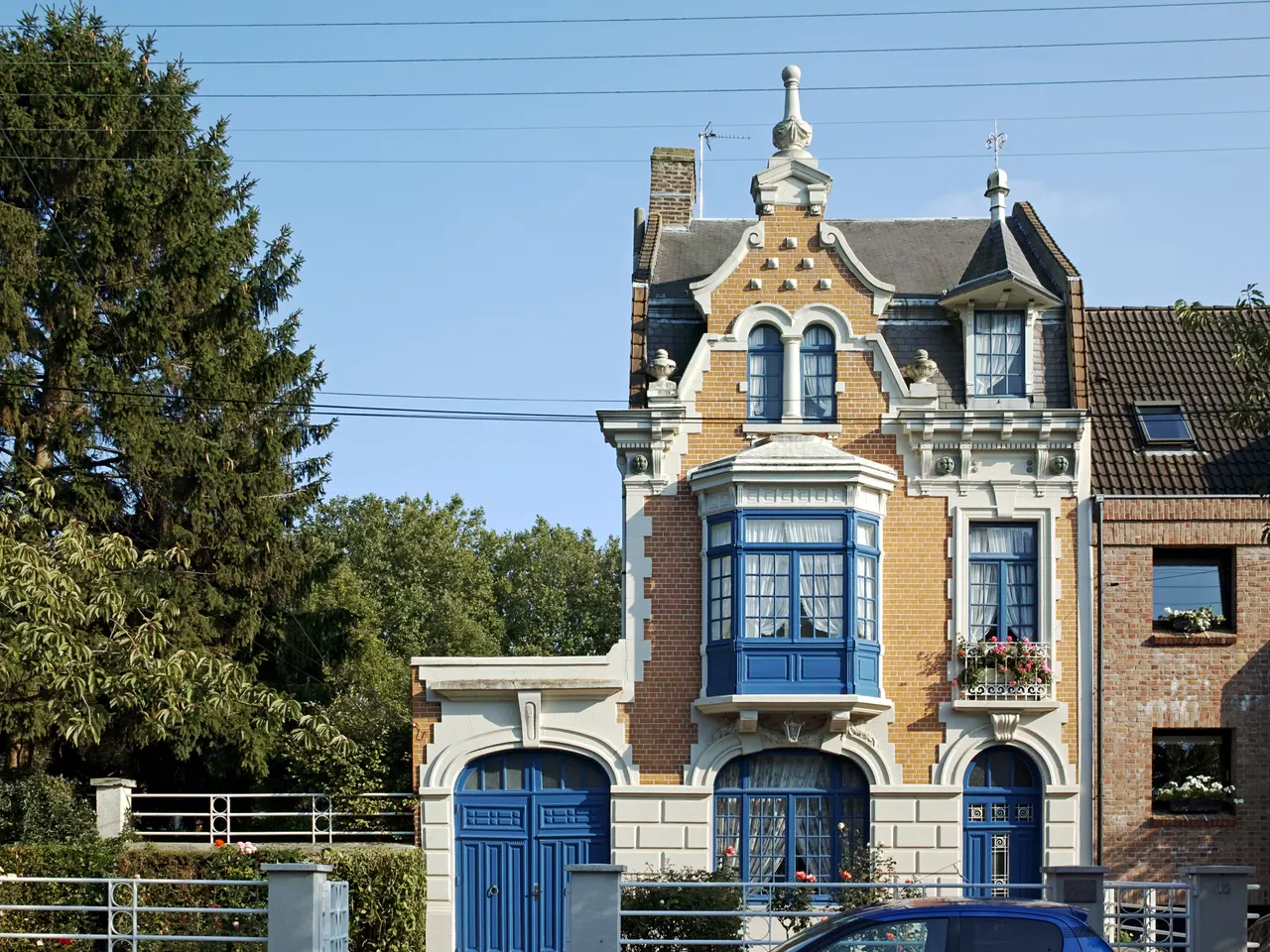 Une maison de ville de briques blondes à bow-window et menuiseries bleues, avenue du Colysée à Lambersart, sous un ciel bleu