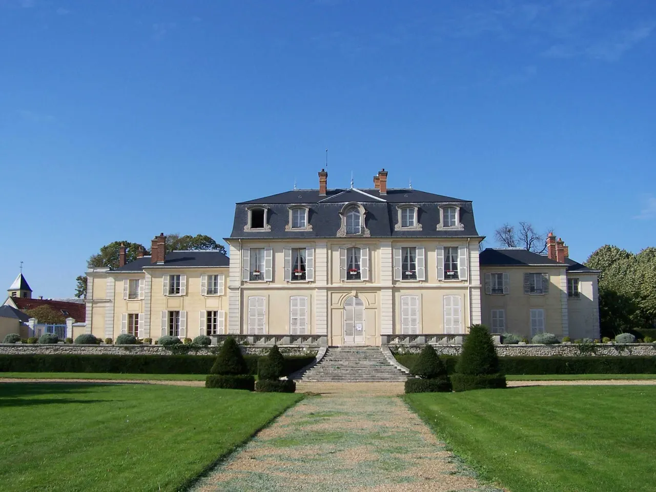 Le château Aubert du Chesnay, façade claire et toit d’ardoise, au bout d’une allée bordée de pelouses et d’ifs taillés