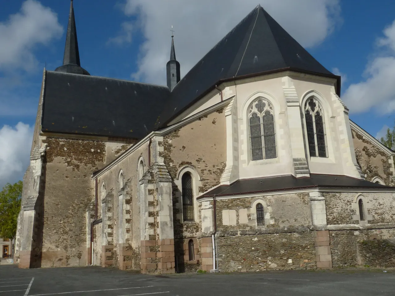 Le chevet de l’église Saint-Michel du May-sur-Èvre, murs de pierre et toits d’ardoise sous un ciel bleu