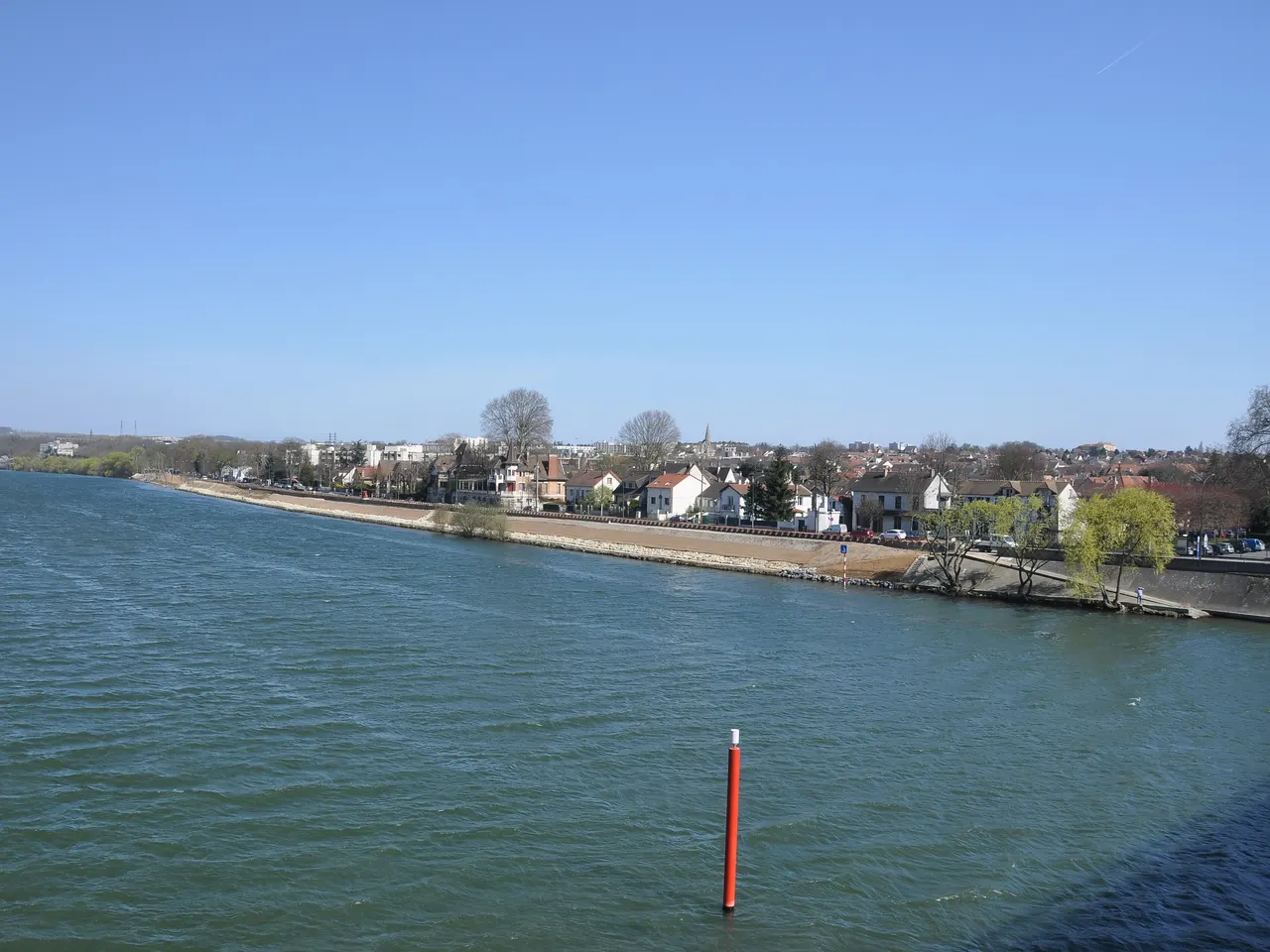 La Seine au Pecq, ses berges aménagées et les maisons de la rive sous un ciel bleu, avec une balise rouge dans l’eau