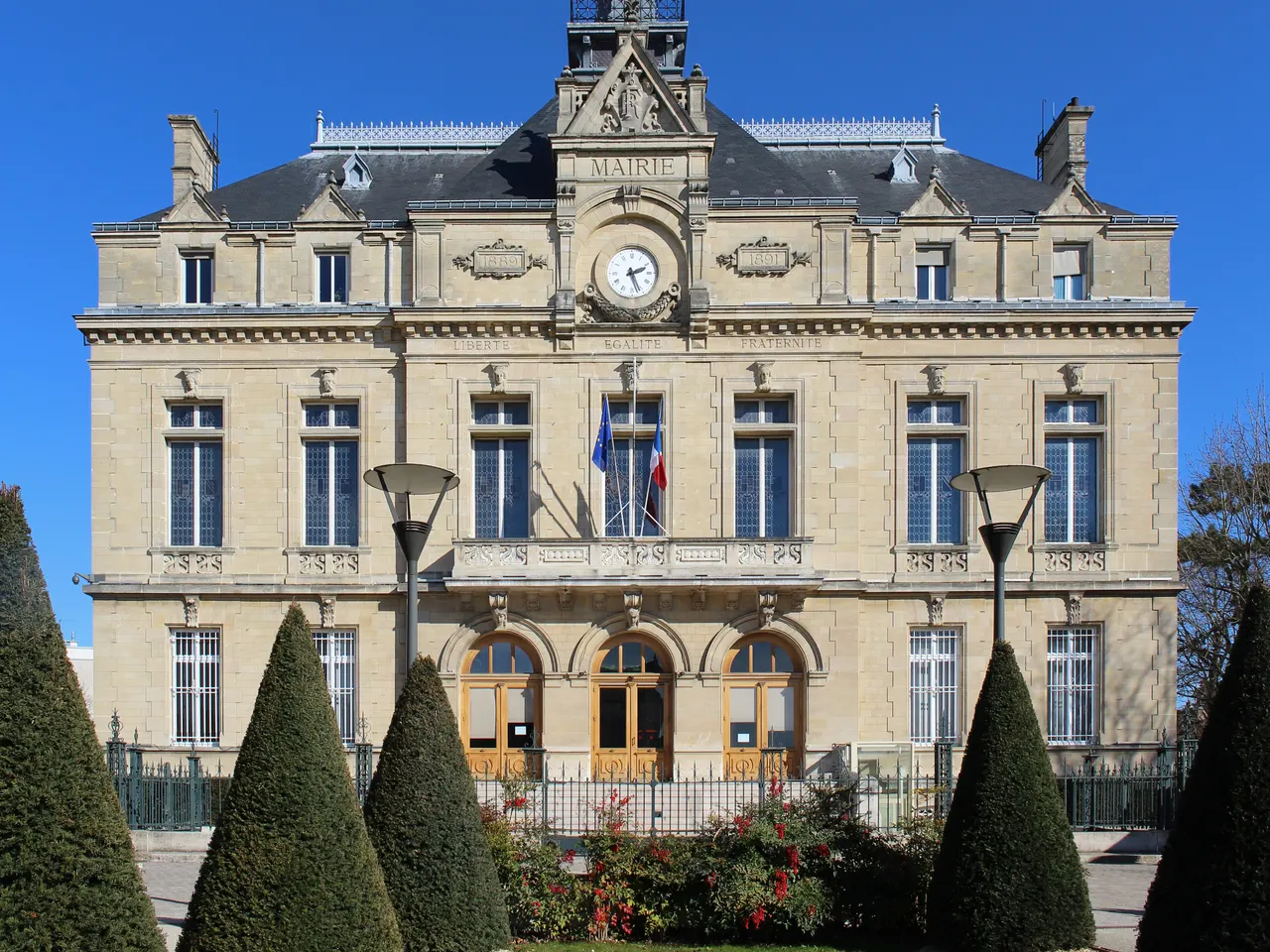 Mairie du Perreux-sur-Marne, façade en pierre à horloge et balcon, précédée d’ifs taillés en cône et de massifs fleuris, ciel bleu