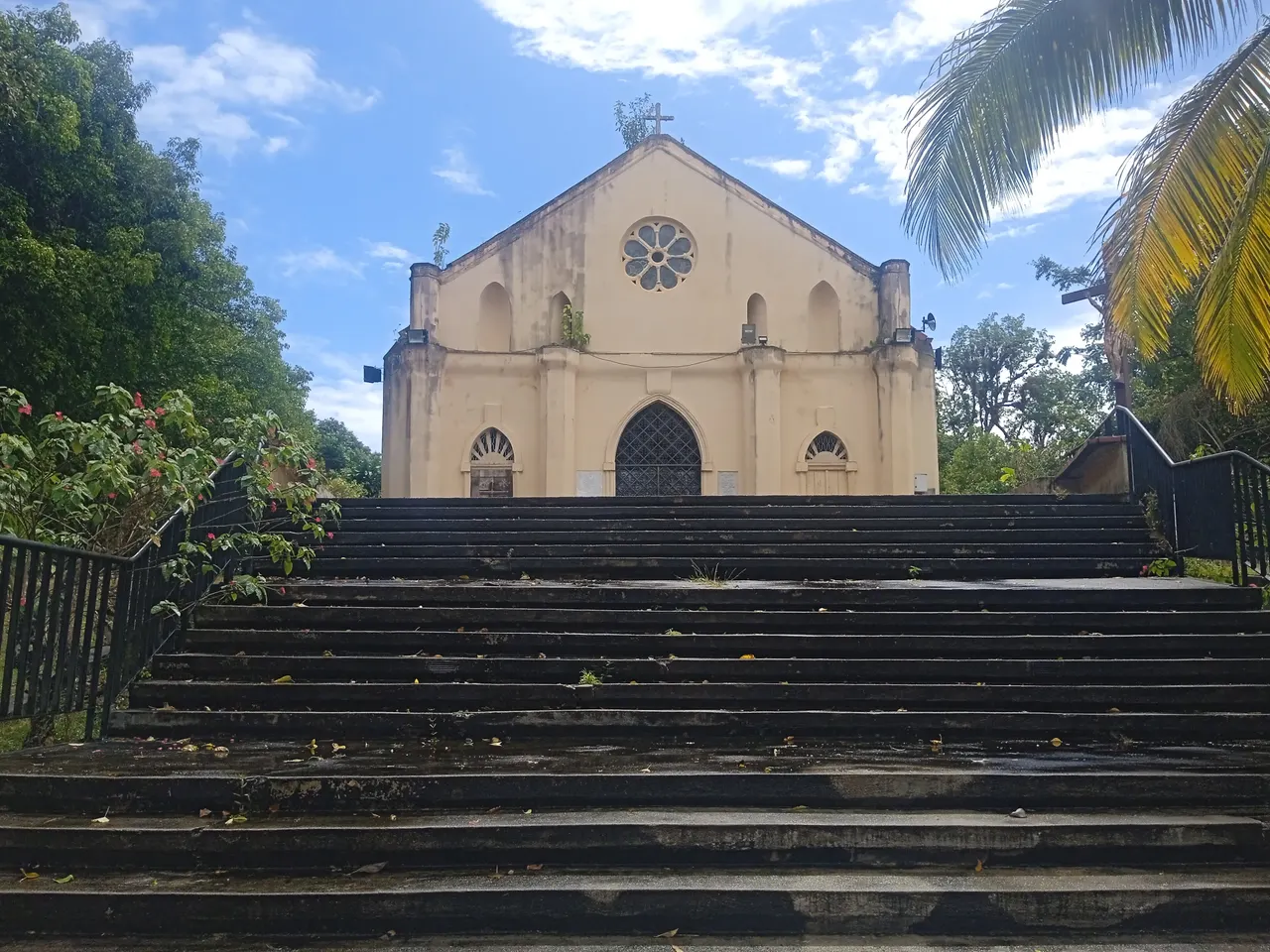 Le grand escalier qui monte à la chapelle Notre-Dame-de-la-Guadeloupe, sur le morne Calvaire aux Abymes, entre les arbres et les palmes.