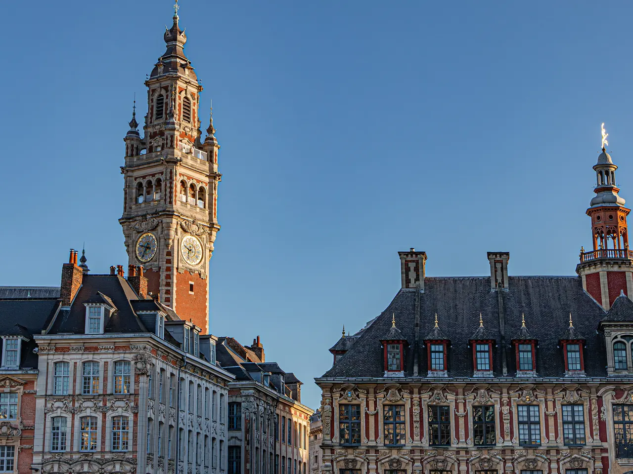 Le beffroi de la Chambre de commerce de Lille et les toits ornés de la Vieille Bourse, éclairés par une lumière dorée sous un ciel bleu