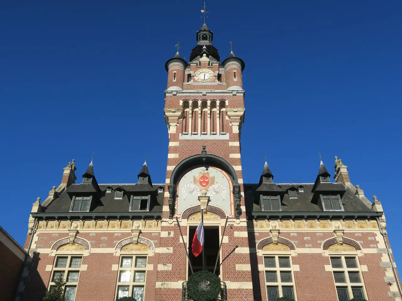 Le beffroi néo-flamand de l’hôtel de ville de Loos, en briques rouges et pierre claire, avec son horloge et ses tourelles sous un ciel bleu intense