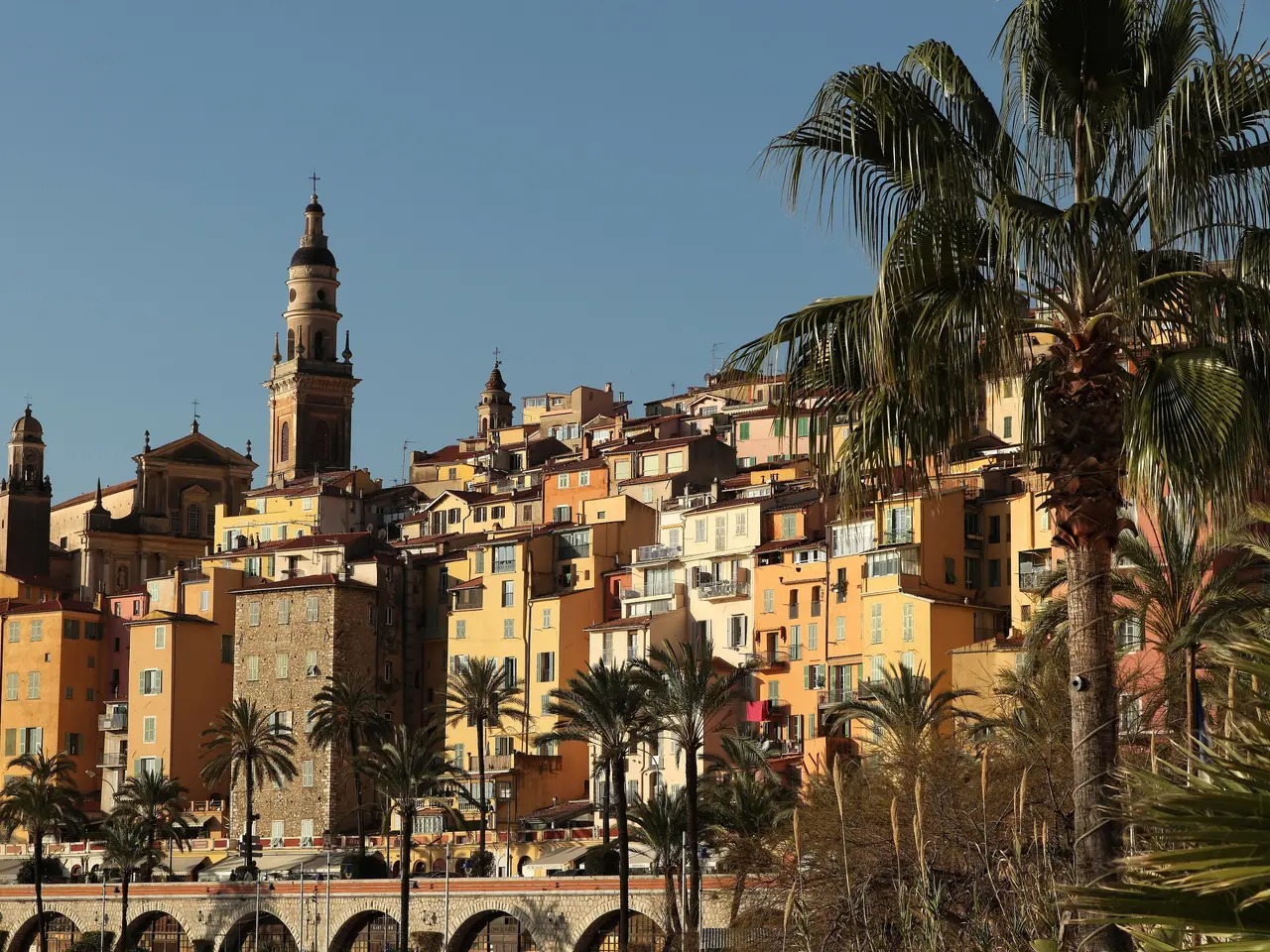 La vieille ville de Menton, ses façades ocre étagées sur la colline et le clocher de la basilique Saint-Michel-Archange, encadrées de palmiers