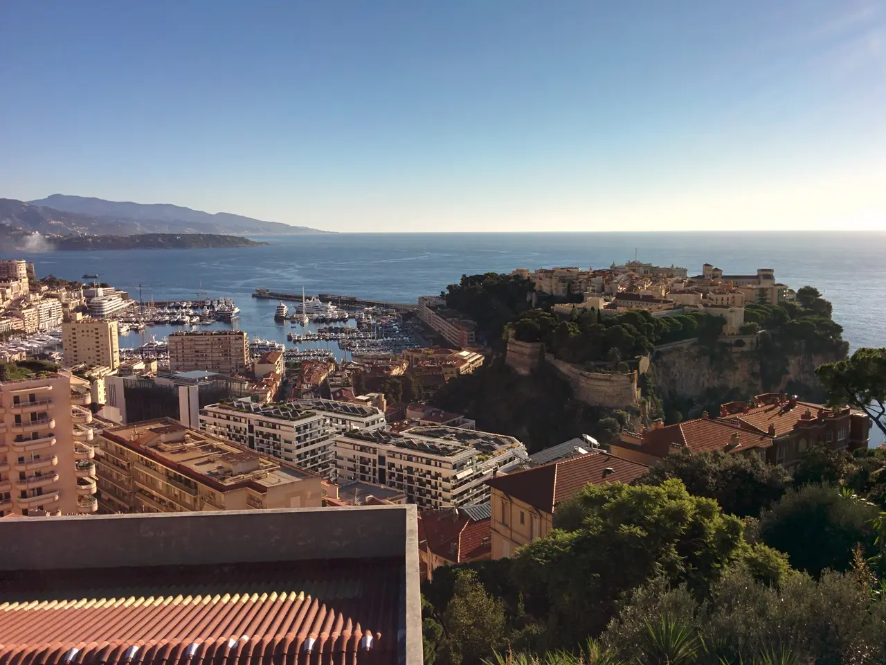 Le Rocher de Monaco et le port Hercule vus des hauteurs, avec des immeubles au premier plan et la Méditerranée au fond