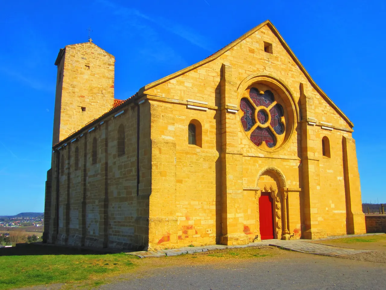 L’ancienne église romane du prieuré de Mont-Saint-Martin, en pierre jaune avec sa rosace et sa porte rouge, sous un ciel bleu profond
