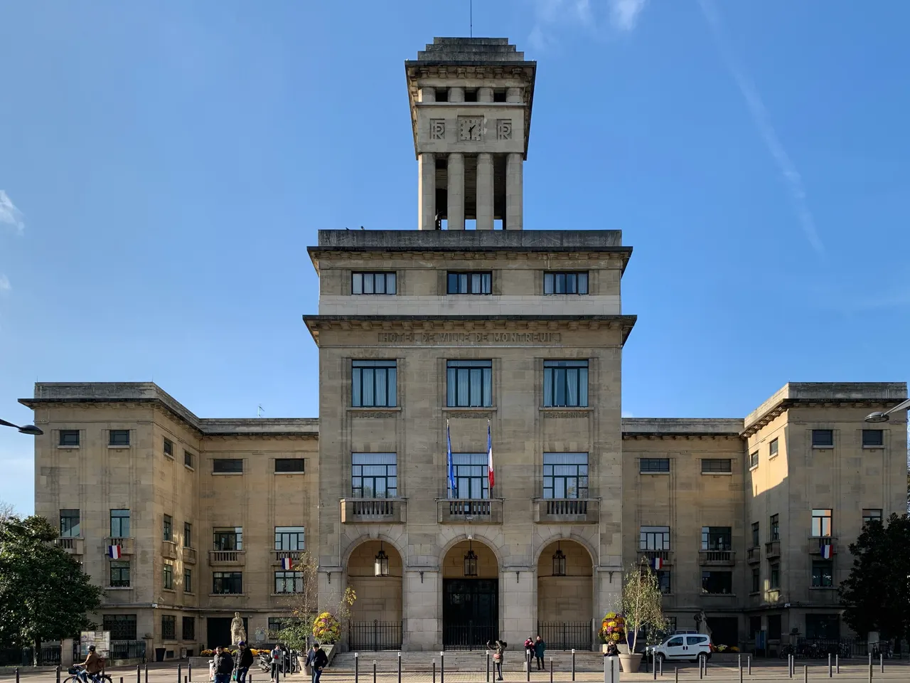L’hôtel de ville de Montreuil, façade de pierre claire à trois arcades surmontée d’une haute tour carrée à horloge, sous un ciel bleu.
