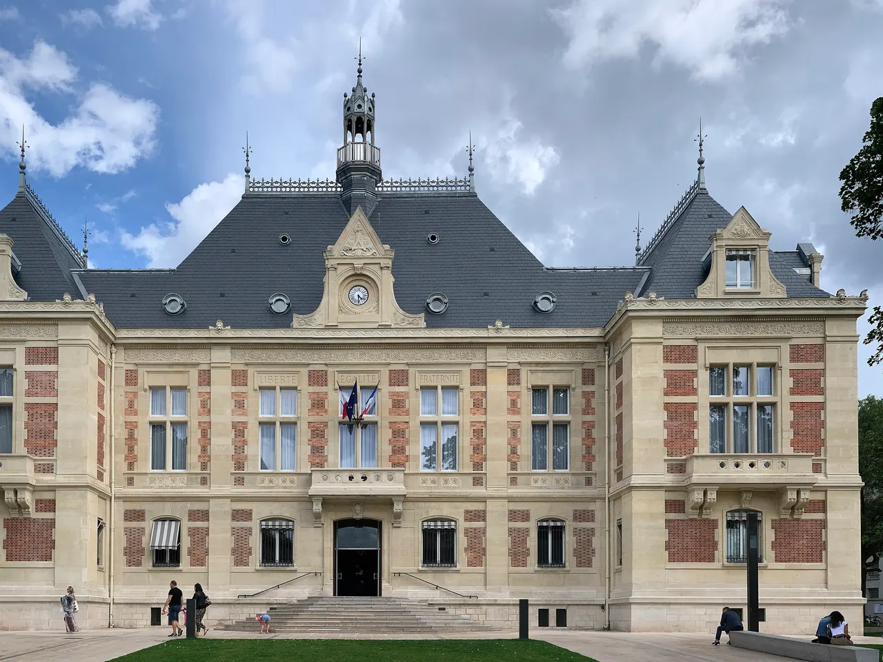 L’hôtel de ville de Montrouge, en pierre et brique, avec son horloge et son campanile, sous un ciel nuageux.