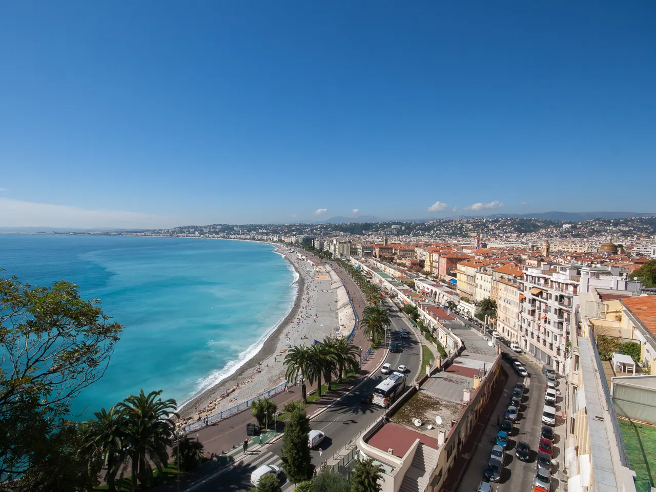 La baie des Anges et la promenade des Anglais vues des hauteurs, entre la mer turquoise, les palmiers et les toits de Nice.