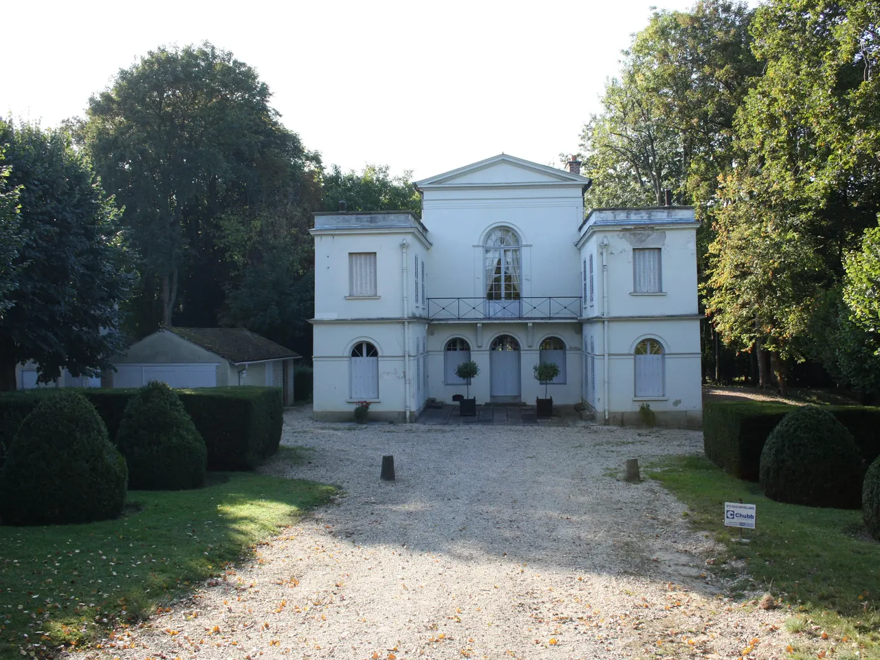 Le temple de la Gloire à Orsay, pavillon néoclassique blanc à fronton, au fond d’une allée de gravier bordée de buis et de grands arbres.