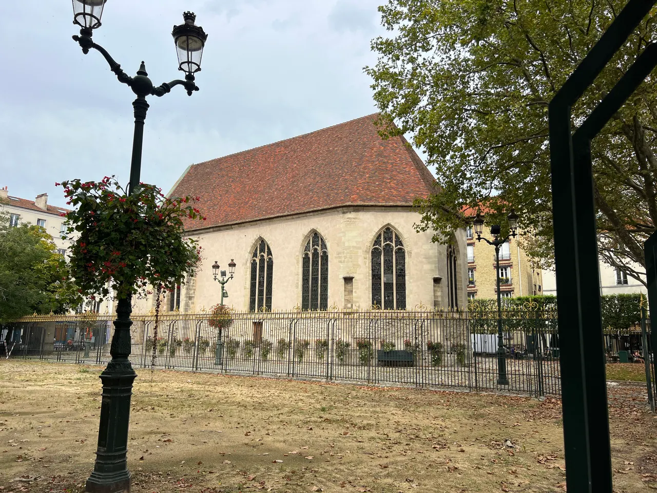 L’église Notre-Dame-de-Pitié de Puteaux, nef gothique au toit de tuiles rouges derrière une grille dorée, vue depuis un square.