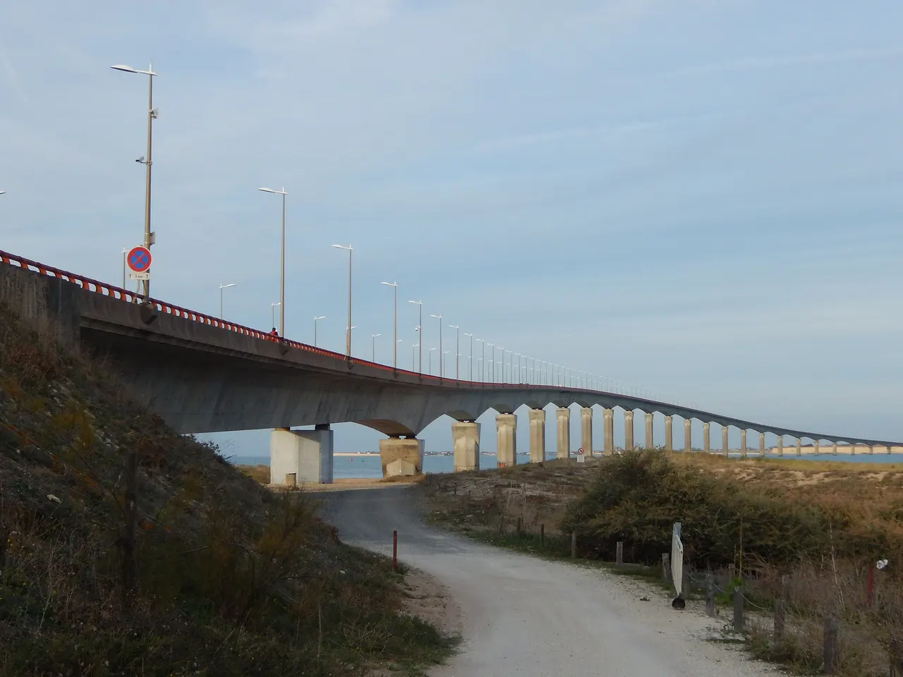 Le pont de l’île de Ré vu depuis Rivedoux-Plage, ses piles alignées au-dessus de la mer, avec un chemin qui descend entre les dunes.