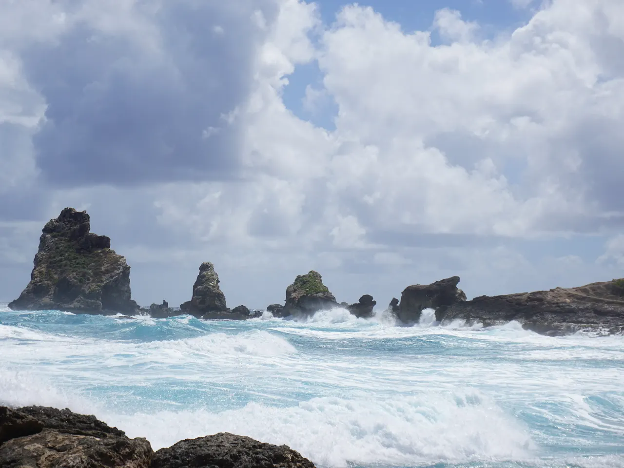 Les rochers de la pointe des Châteaux, à Saint-François, émergent d’une mer agitée et blanche d’écume, sous un ciel chargé de nuages.