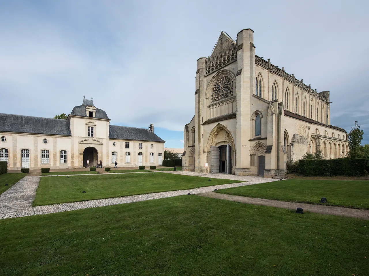 L’abbatiale gothique de l’abbaye d’Ardenne et un bâtiment conventuel à porche, autour d’une cour engazonnée, à Saint-Germain-la-Blanche-Herbe