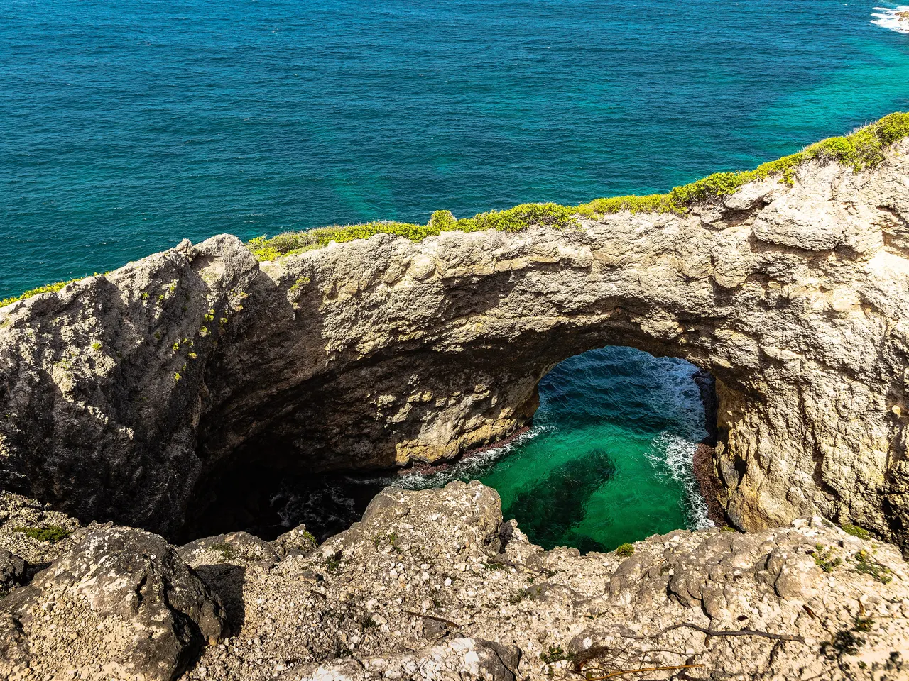 La Gueule Grand Gouffre à Saint-Louis : une arche de roche claire au-dessus d’un bassin d’eau émeraude, au bord de la falaise qui domine la mer turquoise