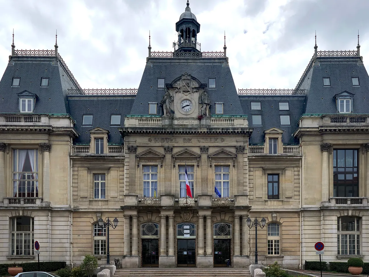 Façade de l’hôtel de ville de Saint-Maur-des-Fossés, hauts toits d’ardoise, horloge sculptée et campanile, sous un ciel nuageux