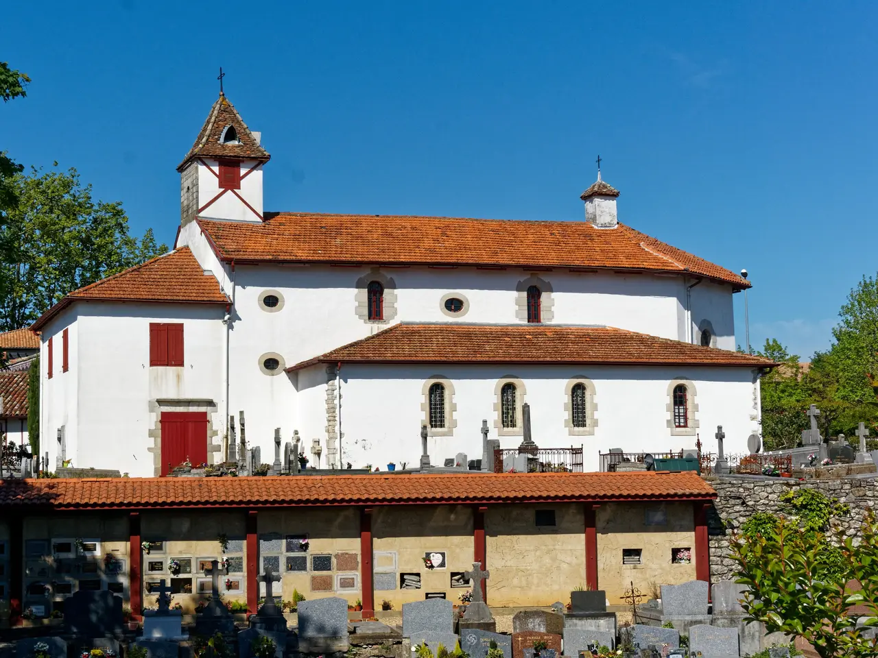 L’église Saint-Pierre de Saint-Pierre-d’Irube, blanche aux volets rouges, au-dessus de son cimetière et de sa galerie couverte