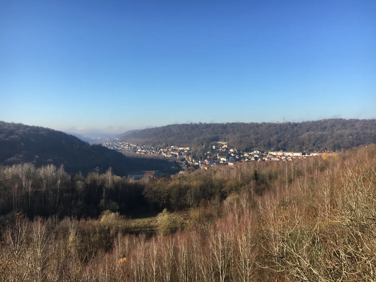 Vue plongeante sur les maisons de Saulnes au creux d’une vallée boisée, en hiver, sous un ciel bleu dégagé.