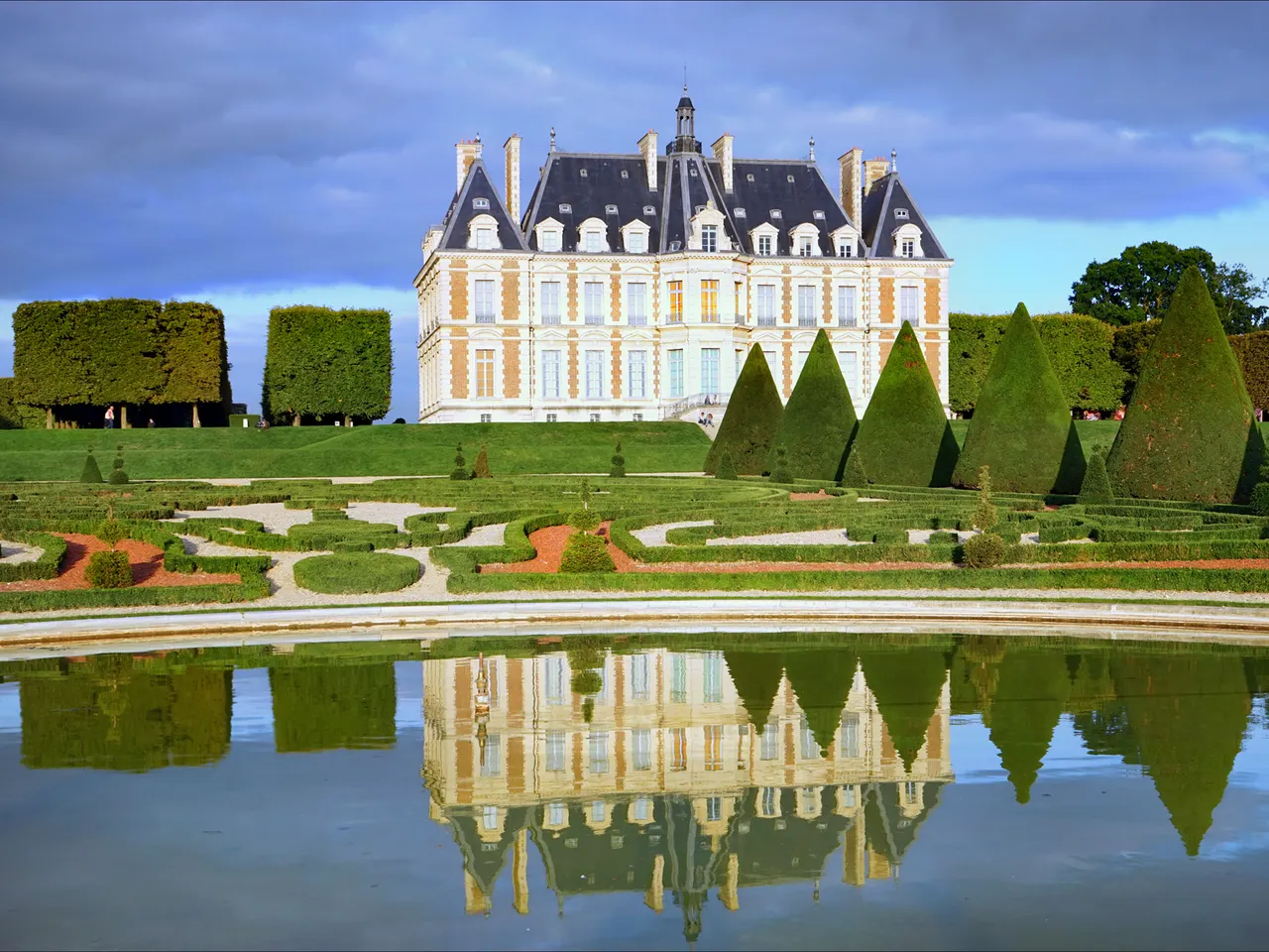 Le château de Sceaux et ses ifs taillés en cône, reflétés dans un bassin du parc à la française.