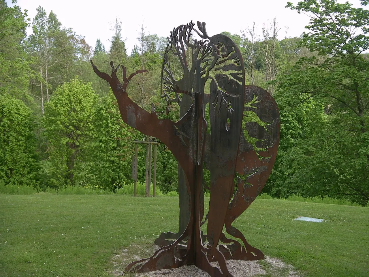 La sculpture en métal découpé « Le baobab et le pommier », dressée sur une pelouse bordée d’arbres, à Verson