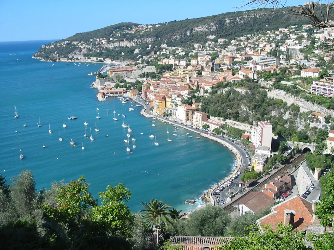 La rade de Villefranche-sur-Mer vue d’en haut : voiliers au mouillage, vieille ville aux façades colorées et citadelle au bord de l’eau.