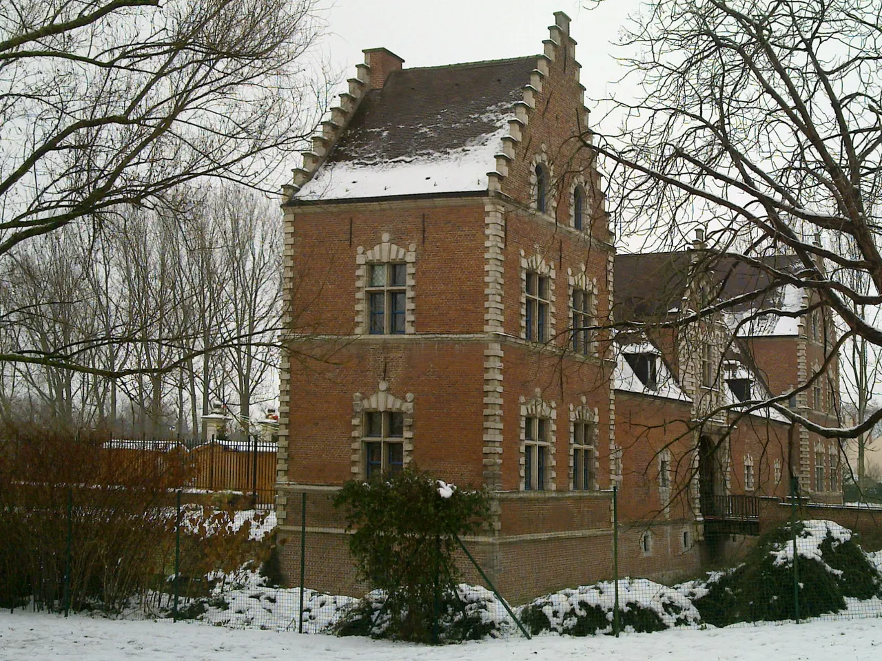Le château de Flers, demeure flamande de briques rouges à pignon à gradins, entouré d’arbres nus et de neige