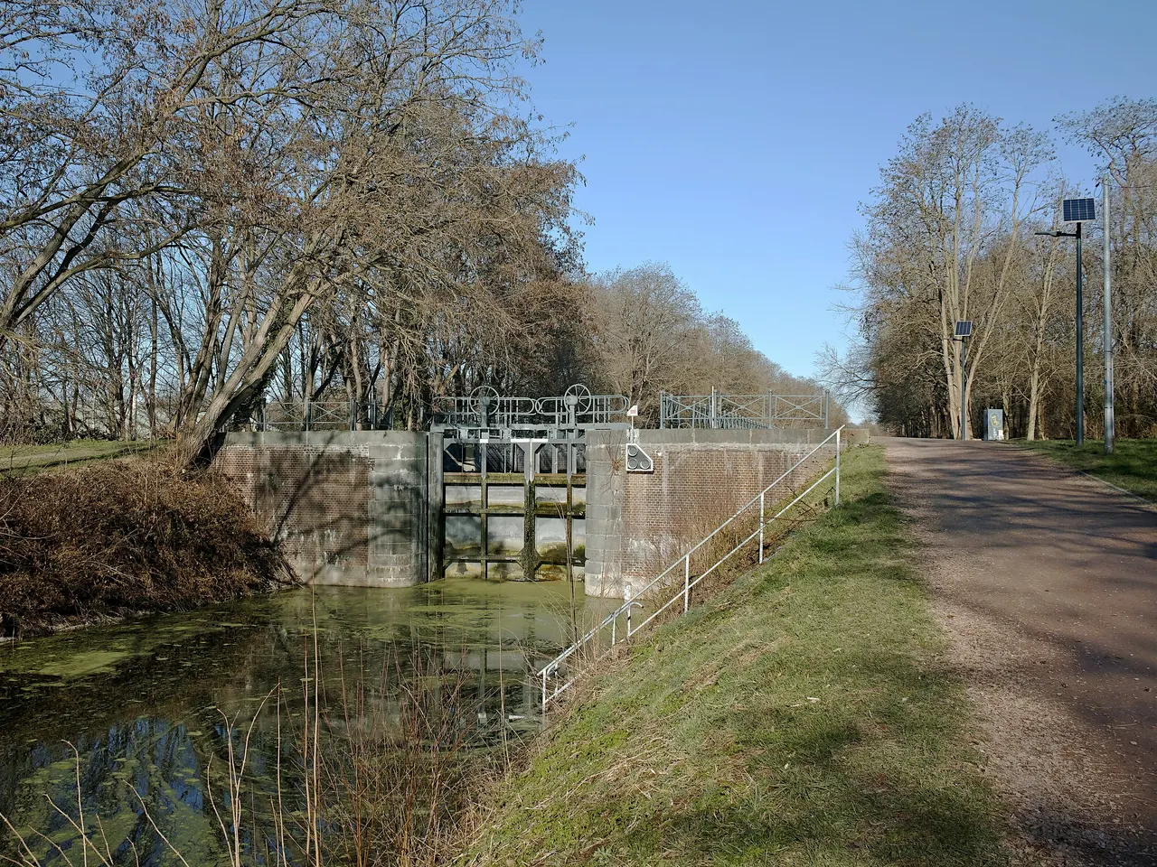 L’écluse du Noir Bonnet à Wasquehal, ses portes et ses murs de briques au bord d’un canal, à côté d’un chemin bordé d’arbres en hiver